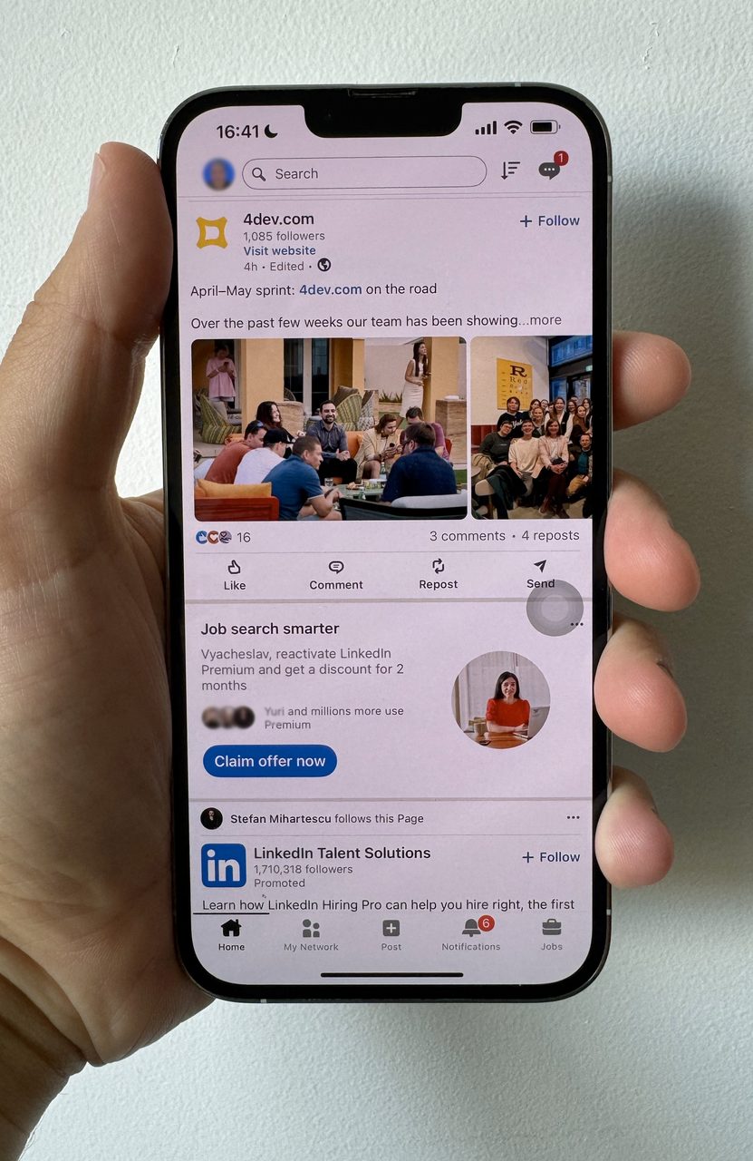 Hand holding an iPhone showing a LinkedIn feed with a company post and inline ad.