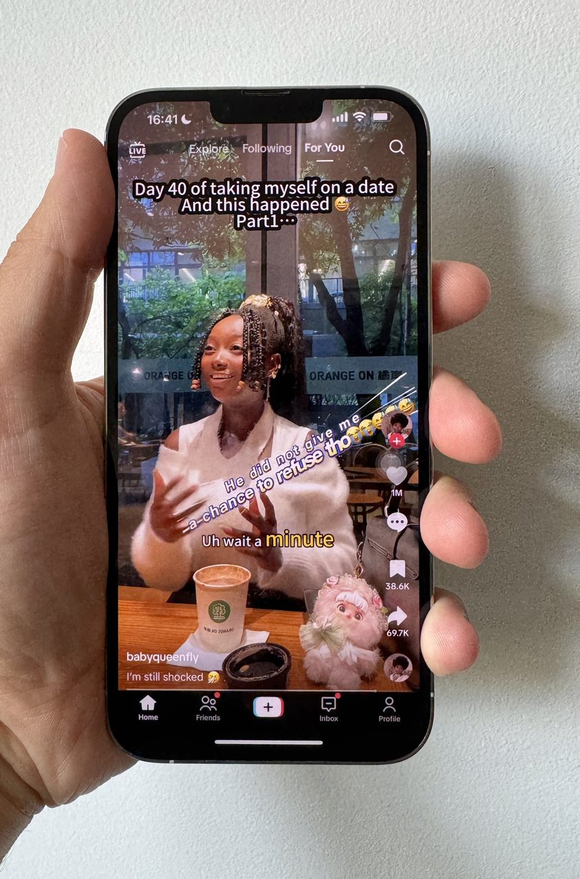 Hand holding an iPhone showing the TikTok For You feed in active use.