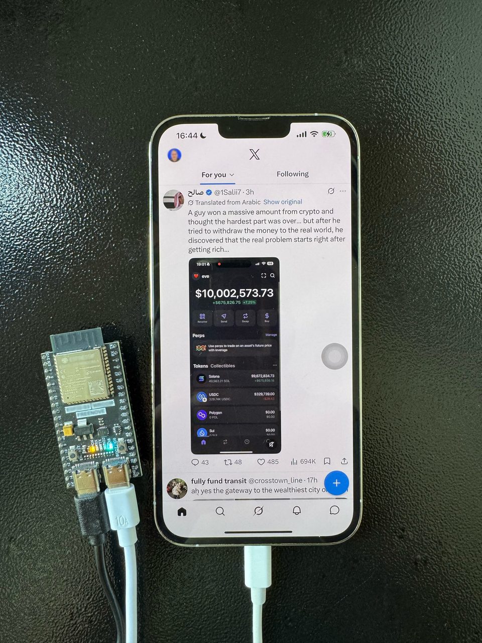 Self-hosted iPhone on a desk connected via USB-C to a BoostLayer controller board, with X open on screen.